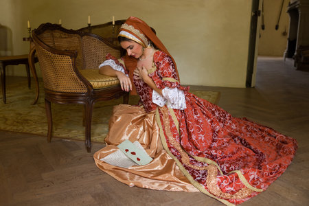 Young woman in medieval renaissance costume and French hood sitting on the floor holding a letter