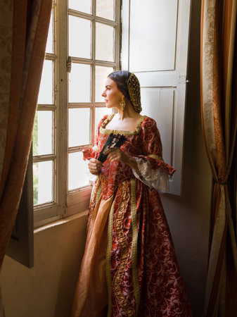 Woman wearing authentic Renaissance costome and headdress standing at her window in a medieval castleの写真素材