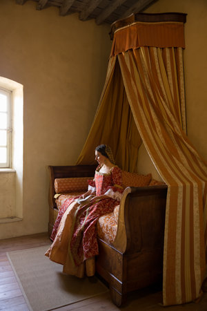 Renaissance lady in late medieval gown sitting on a beautiful canopy bed in her castle bedroomの写真素材