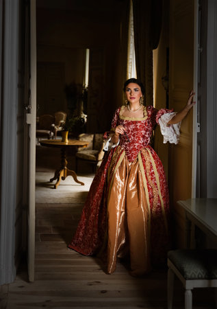 Beautiful woman in late renaissance costume posing between the open doors of a medieval castle.の写真素材