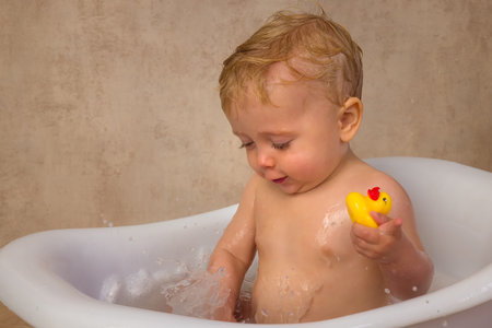 Happy scenes of a little cute baby boy of 12 months old sitting in a vintage white bath tub...