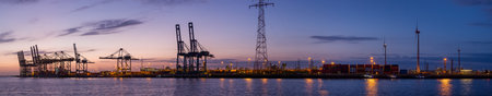 The busy harbour of Antwerp showing a skyline of cranes and container ships at sunsetの写真素材