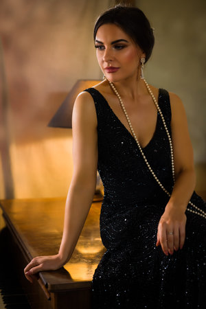 Stunning young woman in black beaded 1920s flapper dress sitting on an old pianoの写真素材