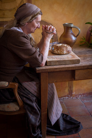 Woman in authentic peasant renaissance costume praying at a table. There is bread on the table.の写真素材
