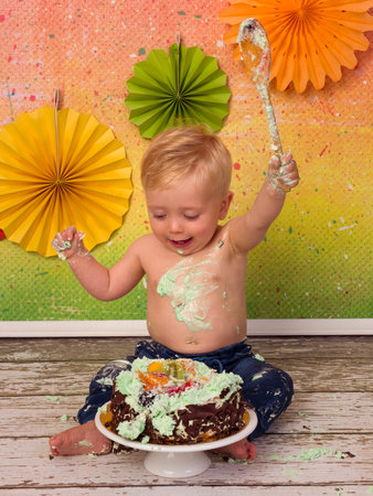 Colorful images shot during the first birthday party of a little blonde boy smashing his birthday cake with wooden spoonsの写真素材