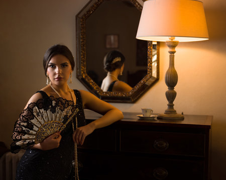 Beautiful woman in black beaded 1920s flapper dress looking into her antique mirrorの写真素材