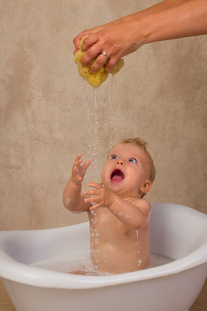 Happy scenes of a little cute baby boy of 12 months old sitting in a vintage white bath tub splashing with water and soapの写真素材