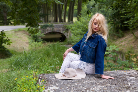 Young pretty blonde woman with vintage hat waiting on rustic bridgeの写真素材