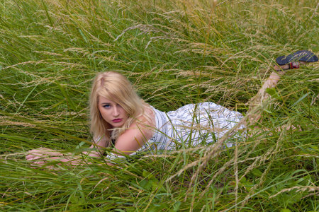 Dreamy young blonde woman relaxing lying down in a meadow with high grassesの写真素材