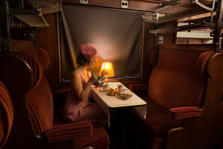 Reenactment scene of a 1920s flapper dress lady enjoying high tea in an authentic 1927 steam train compartmentの写真素材