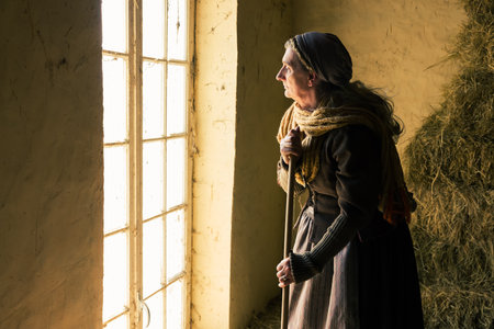 Woman in historical medieval costume working with a broom in a hay shedの写真素材