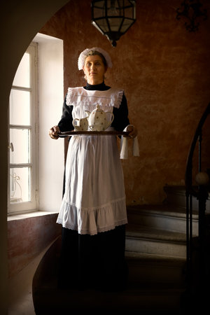 Victorian maid or servant in black dress, lace cap and white apron working in a 19th century interiorの写真素材