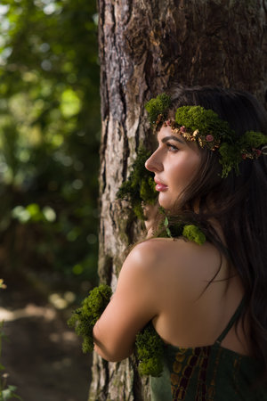 Beautiful young woman in green dress posing as a forest fairy with sheer chiffon fabrics and moss garlandsの写真素材