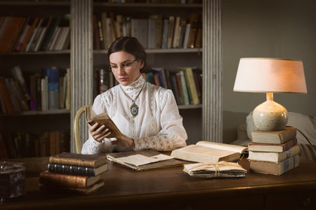 Beautiful lady in Edwardian skirt and high collar lace blouse sitting in the library. She could be a...