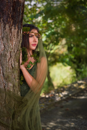 Beautiful young woman in green dress posing as a forest fairy with sheer chiffon fabrics and moss garlandsの写真素材