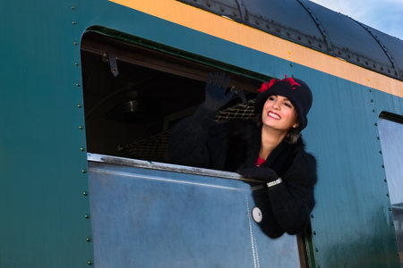 1920s woman wearing fur coat and cloche hat hanging out of the window of an antique train carriageの写真素材