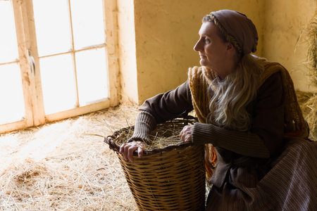Woman in historical medieval costume posing with a wicker basket in a hay barnの写真素材