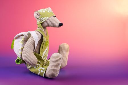 Mouse pupil toy wearing green rompers and back pack sitting on color gradient backgroundの写真素材