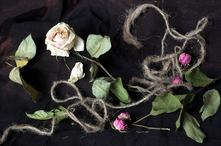 A dry rose is decorated by a hemp rope, dry leaves and small flowers.の写真素材