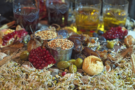 The buckets with grains of wheat and barley are among mung sprouts. These are raisins, figs, pomegranates, olives, dates and ears of wheat. There are four glasses of wine as a background of the still life.の写真素材