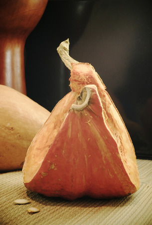 A piece of a pumpkin and a whole pumpkin are on the mat with a tam-tam as background.の写真素材