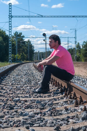 Shot of one man in pink t-shirt sitting on train tracksの写真素材