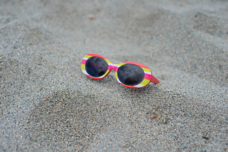 Used childrens striped sunglasses on the sandの写真素材