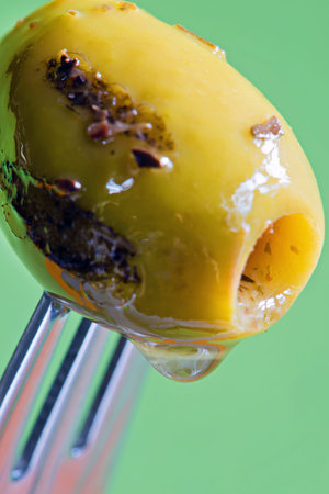 Closeup grilled olive with oil drop on the fork over green backgroundの写真素材