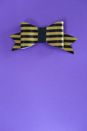 Black and golden striped bow tie over ultra violet background.の写真素材