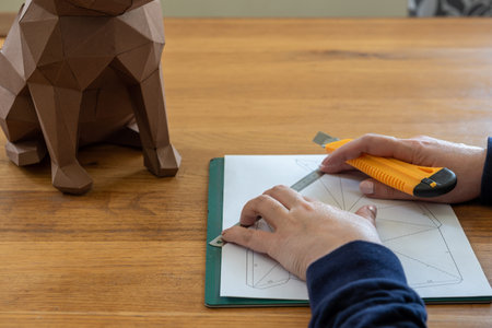 Somebody is making a cube sculpture with paper, linear and knife