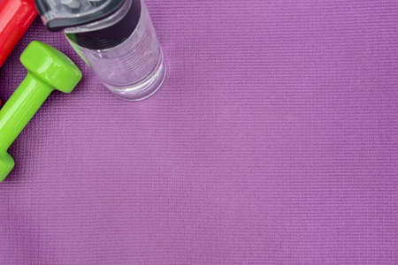 Ladies dumbbells and water bottle over purple fitness mat, top view.の写真素材