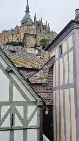 Historic architecture of Mont Saint-Michel viewed from a narrow alley lined with traditional houses on a cloudy dayの写真素材