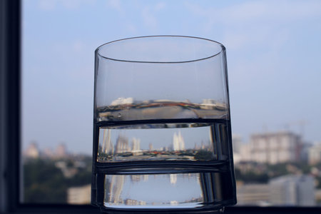 Skyscrapers reflected in a glass of clean water on windowsillの写真素材