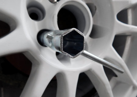 Tubular wrench inside the lug pattern of white car wheel disk closeup