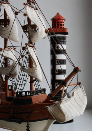 Front Part And Bowsprit Of Toy Masted Ship In Front Of Miniature Beacon Towerの写真素材