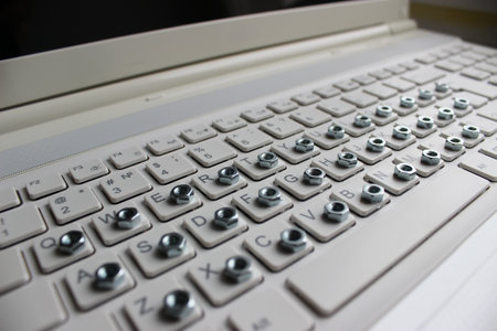 Angled side view of a computer keyboard with an iron nut on each buttonの写真素材
