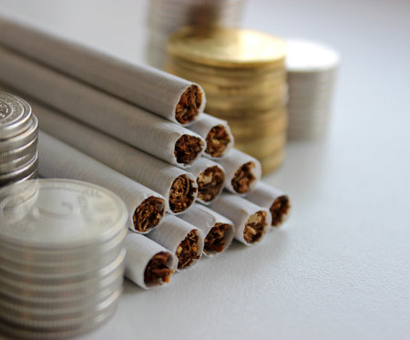 Money in coins and cigarettes in bulk as a symbol of increasing prices for cigarettesの写真素材