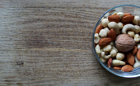 Bowl With Peeled Almonds, Cashew And Hazelnuts And Whole Walnut On A Wooden Board At Side Of Imageの写真素材