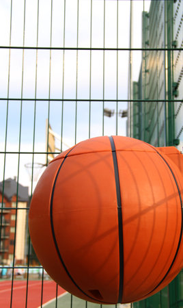 Plastic waste basket in the shape of a basketball ball on a metal grid fenceの写真素材