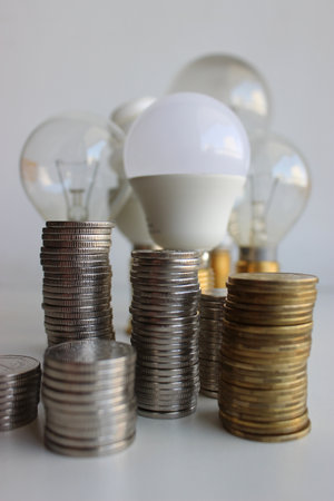 Variety Electric Bulbs And Piles Of Silvery And Brass Coins In A Columns Symbolizing Energy Efficientの写真素材
