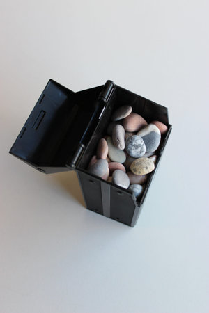 Opened Lid Of Black Box With Colored Sea Stones On White Surface Vertical Stock Photo