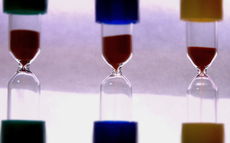 Defocused Shot Of Colorful Time Glasses With Flowing Sand