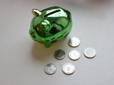 Crack on a Side Of Piggy Bank With Scattered Coins On White Surfaceの写真素材
