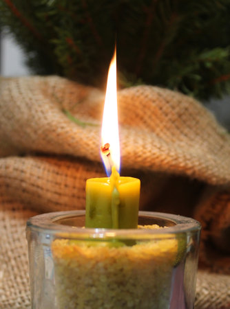 Fire Of Dark Yellow Wax Candle In Glass Candlestick Filled With Grains Near Handmade Burlap Wrappingの写真素材