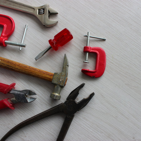 Old but working pliers, a hammer, wire cutters, an adjustable wrench and clamps lie in perfect order on the work tableの写真素材