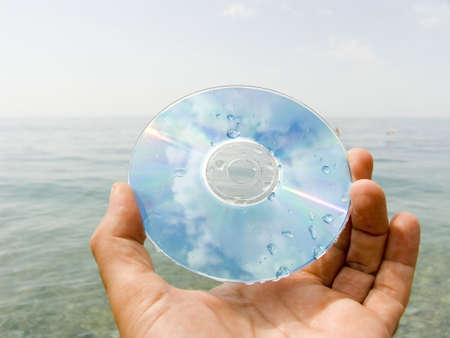 Computer disk in a hand on seacoast in drops of waterの写真素材