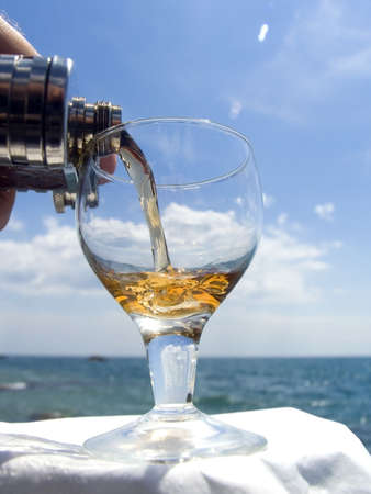 From a flask a wine pour in a wine-glass on a beachの写真素材