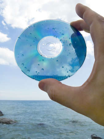 Computer disk in a hand on seacoast in drops of waterの写真素材
