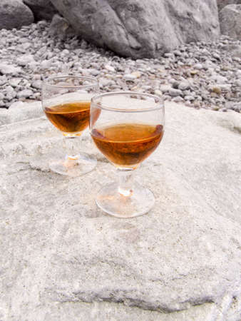 Two wine-glasses with a drink on a sea beach in beams of the sunの写真素材