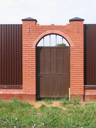 Forged metal gate in the fence with brick pillars with archの写真素材